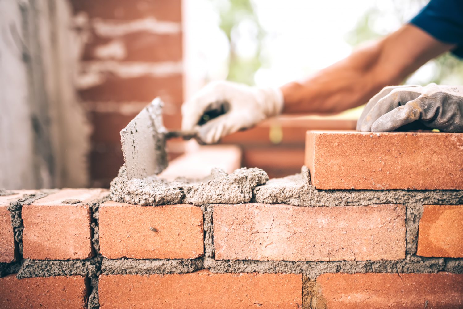 Wallpaper image showing the construction of a brick wall using mortar and a spatula.